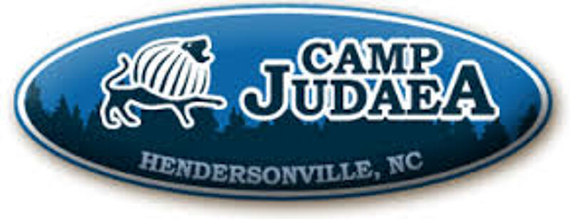 The image is a logo for Camp Judaea, located in Hendersonville, NC. The logo features a blue oval with a stylized lion and trees in the background. The words "Camp Judaea" are prominently displayed in a stylized font. The logo gives a sense of a summer camp in a natural setting.